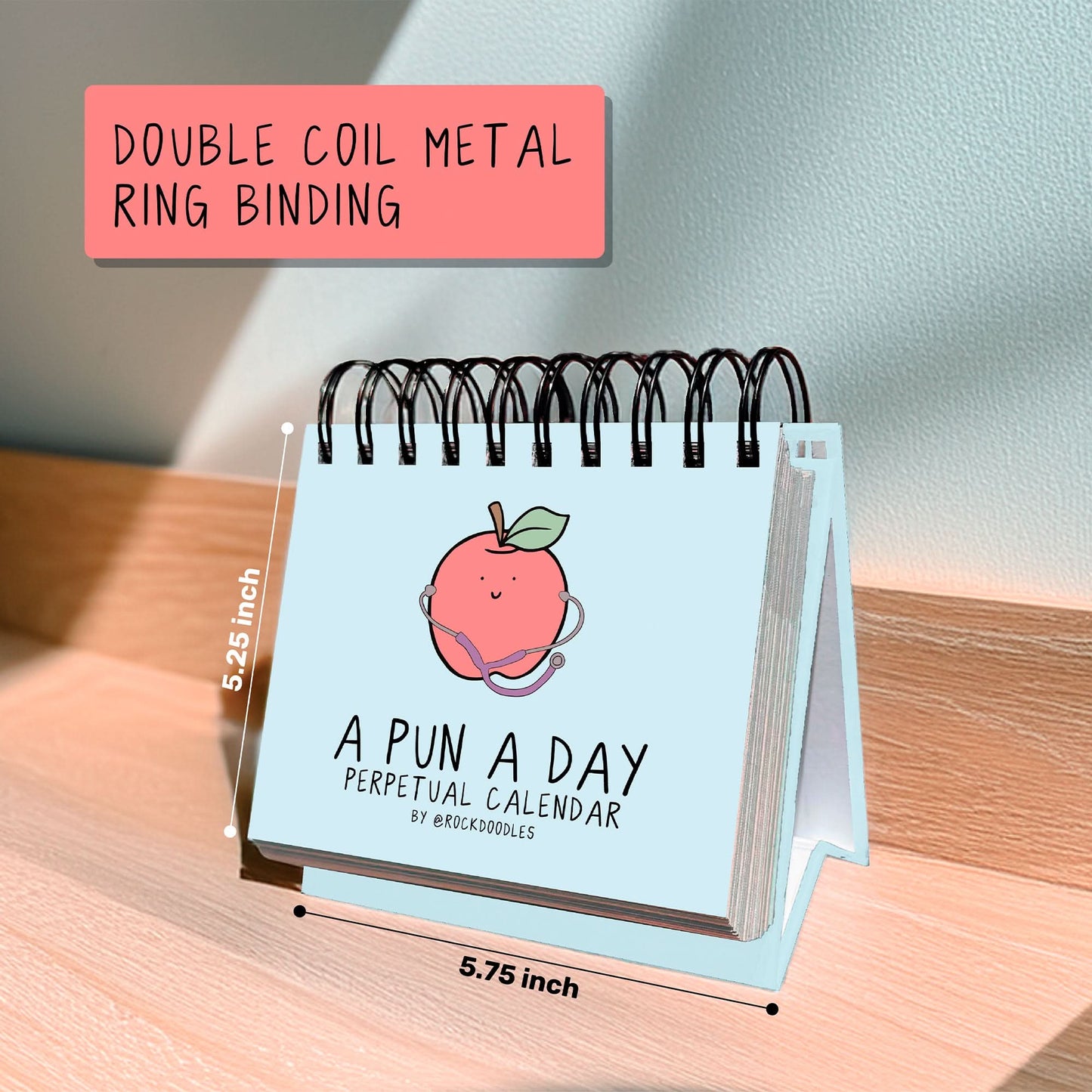 The rockdoodles "A Pun A Day Perpetual Calendar" is a small desktop calendar (5.25 x 5.75 in) with double coil metal binding and a peach cover—ideal for daily pun lovers and wordplay gift seekers.