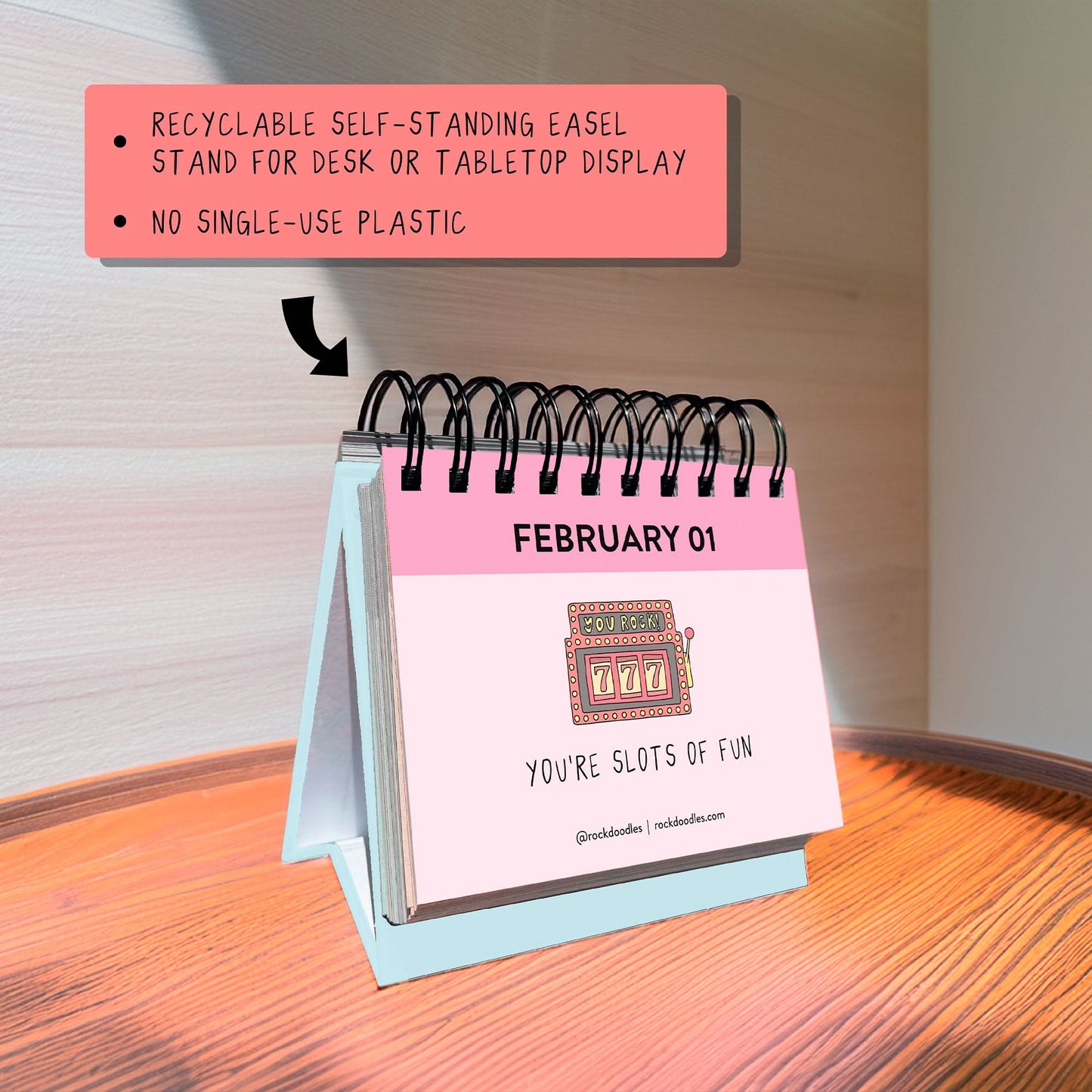 The rockdoodles "A Pun A Day Perpetual Calendar" is a small spiral-bound desk calendar, shown on a wooden surface with February 1 featuring a slot machine and the pun "YOU'RE SLOTS OF FUN”—a fun gift for pun lovers.