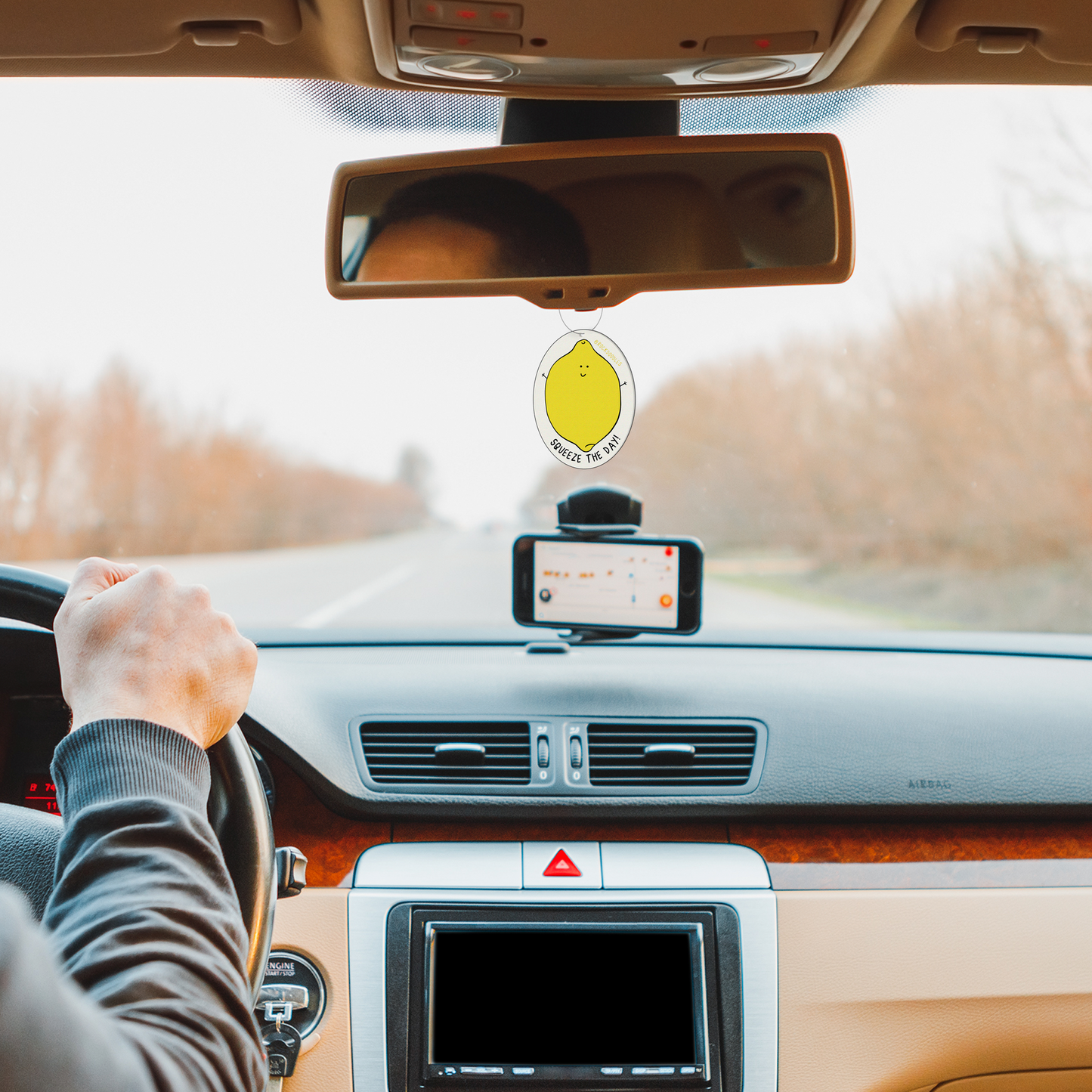 A man driving a car with a rockdoodles Squeeze The Day (2-Pack) Punny Air Freshener - Lemon Scent.