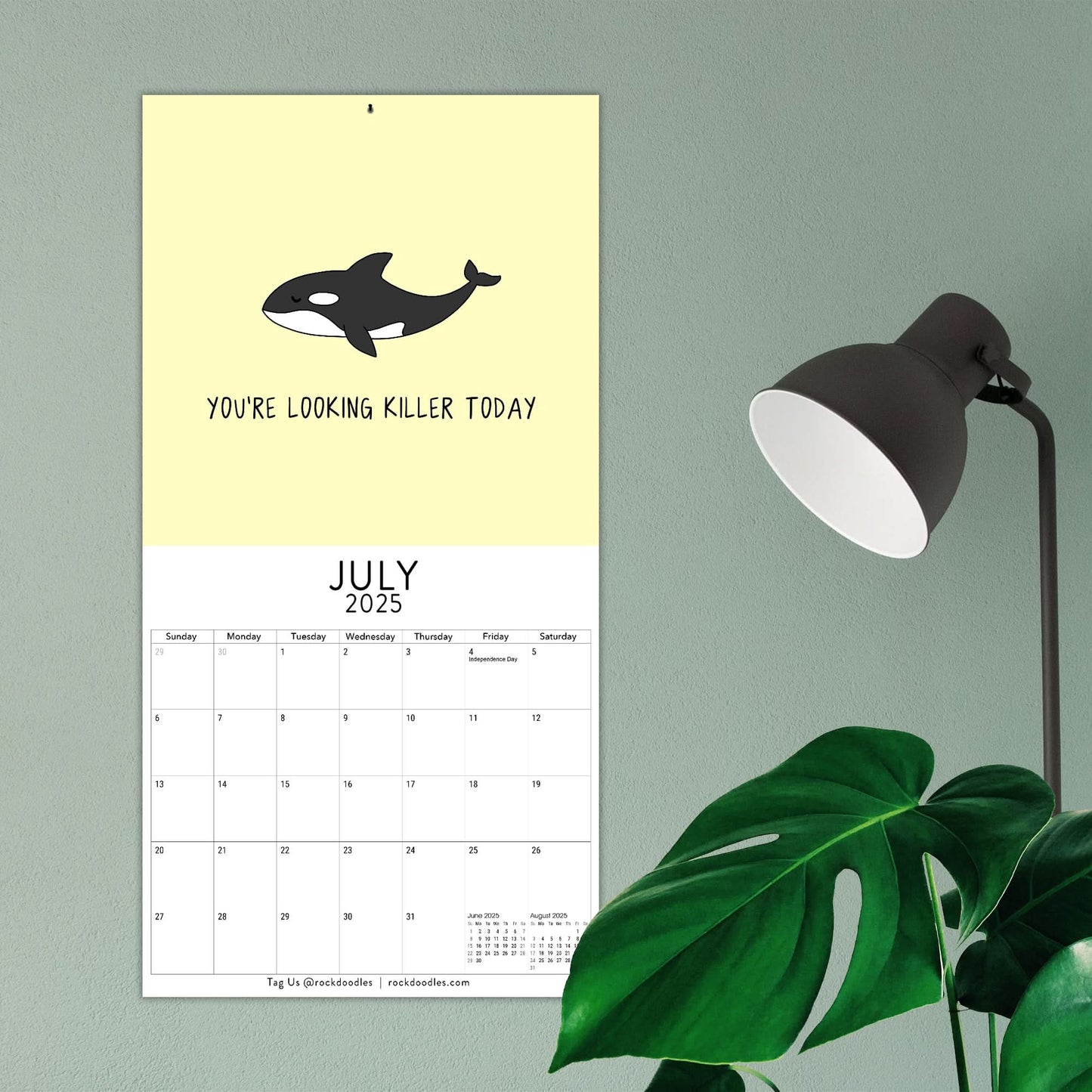 Set to July 2025, the "You've Got To Be Yolking" wall calendar from rockdoodles features an illustration of an orca with the text "You're looking killer today." Nearby, you'll find a black lamp and green plant. This Rockdoodles calendar showcases vibrant design and pun-filled fun.