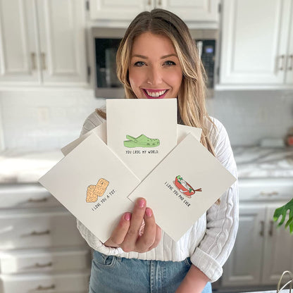 A woman holding up a set of rockdoodles' Wheelie Great Birthday cards with a crocodile on them.