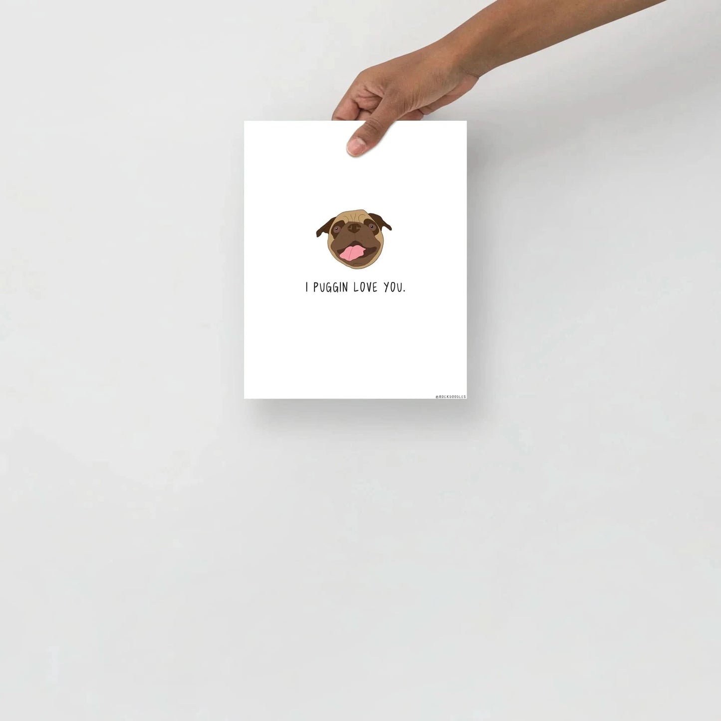 A hand holding a piece of rockdoodles matte paper with a Puggin Love You Print.