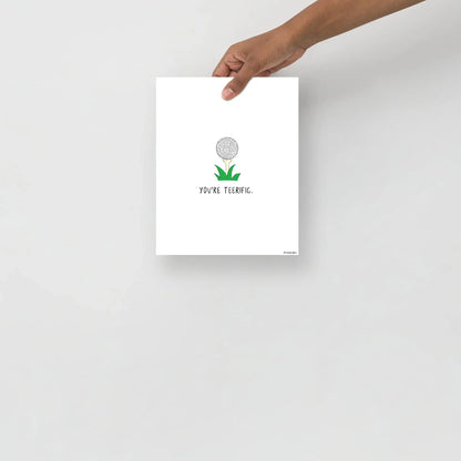 A person holding up a rockdoodles Teerific Print with a green plant on it.