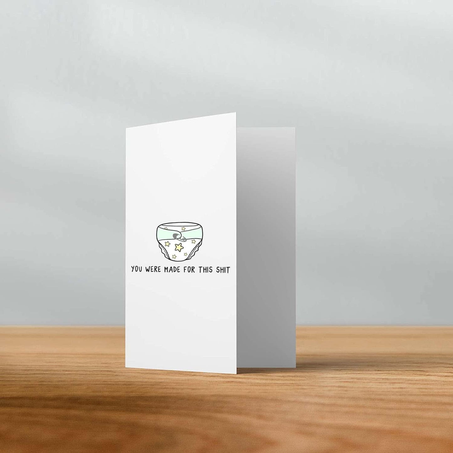 A "Made For This Shit Card" by rockdoodles is displayed on a wooden surface, featuring a simple line drawing of a bowl with stars and the text printed below the image. It comes BLANK INSIDE for your personalized message and includes a natural envelope.