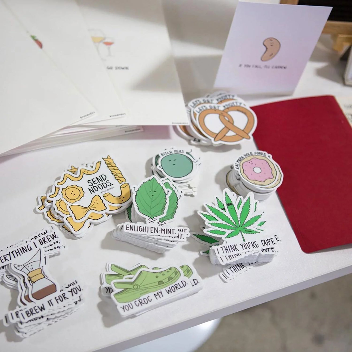 Assorted novelty stickers with humorous text and illustrations, a red envelope, and a greeting card on a display table.