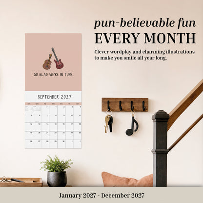 Add a playful twist to your home with the rockdoodles 2027 Wall Calendar "You've Got To Be Yolking"—a pun calendar featuring a delightful egg-themed design and humorous wordplay. This funny wall calendar is pictured hanging above a shelf with hooks, keys, and a potted plant on a staircase wall, bringing cheerful charm and lighthearted fun to your daily routine.