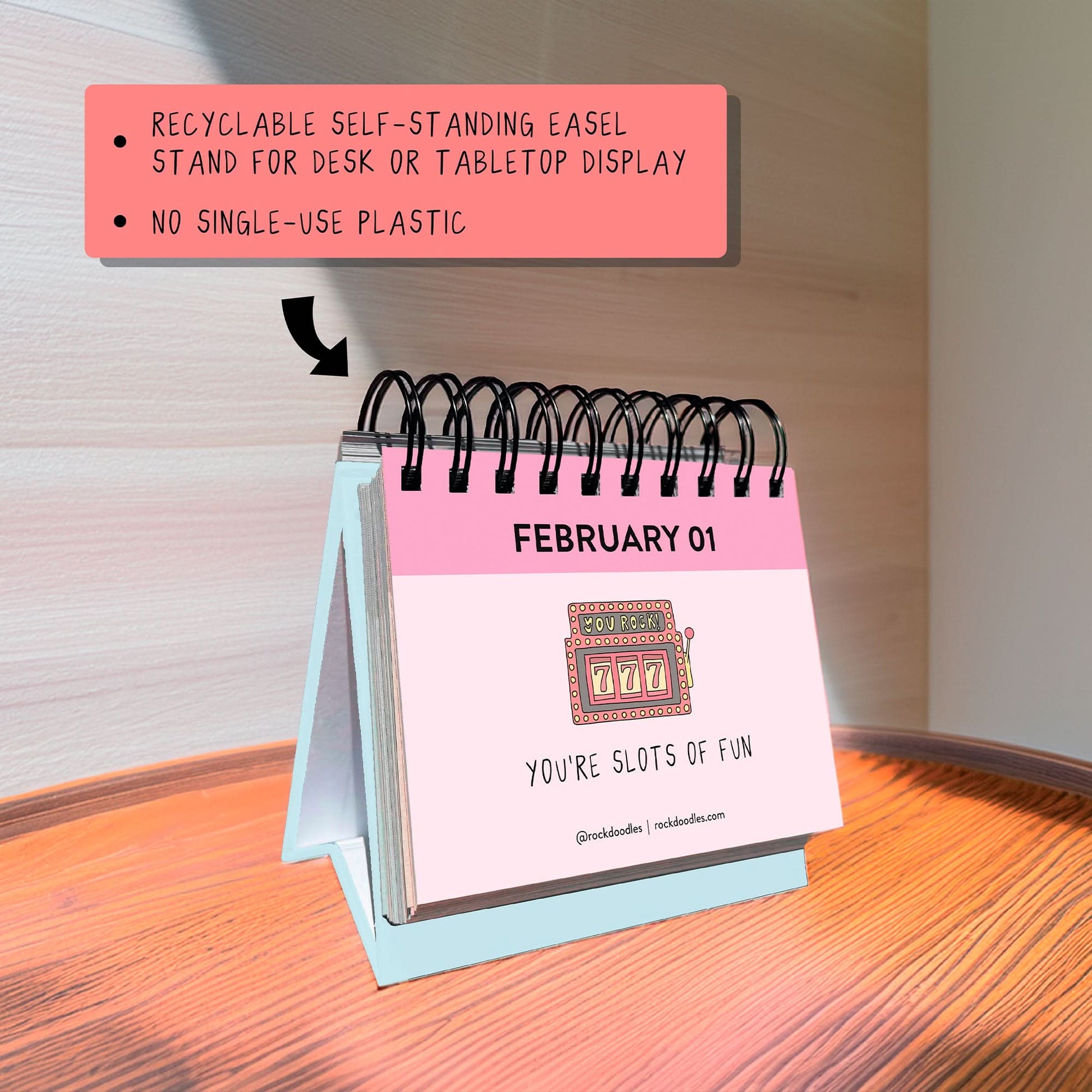 The rockdoodles "A Pun A Day Perpetual Calendar" is a small spiral-bound desk calendar, shown on a wooden surface with February 1 featuring a slot machine and the pun "YOU'RE SLOTS OF FUN”—a fun gift for pun lovers.