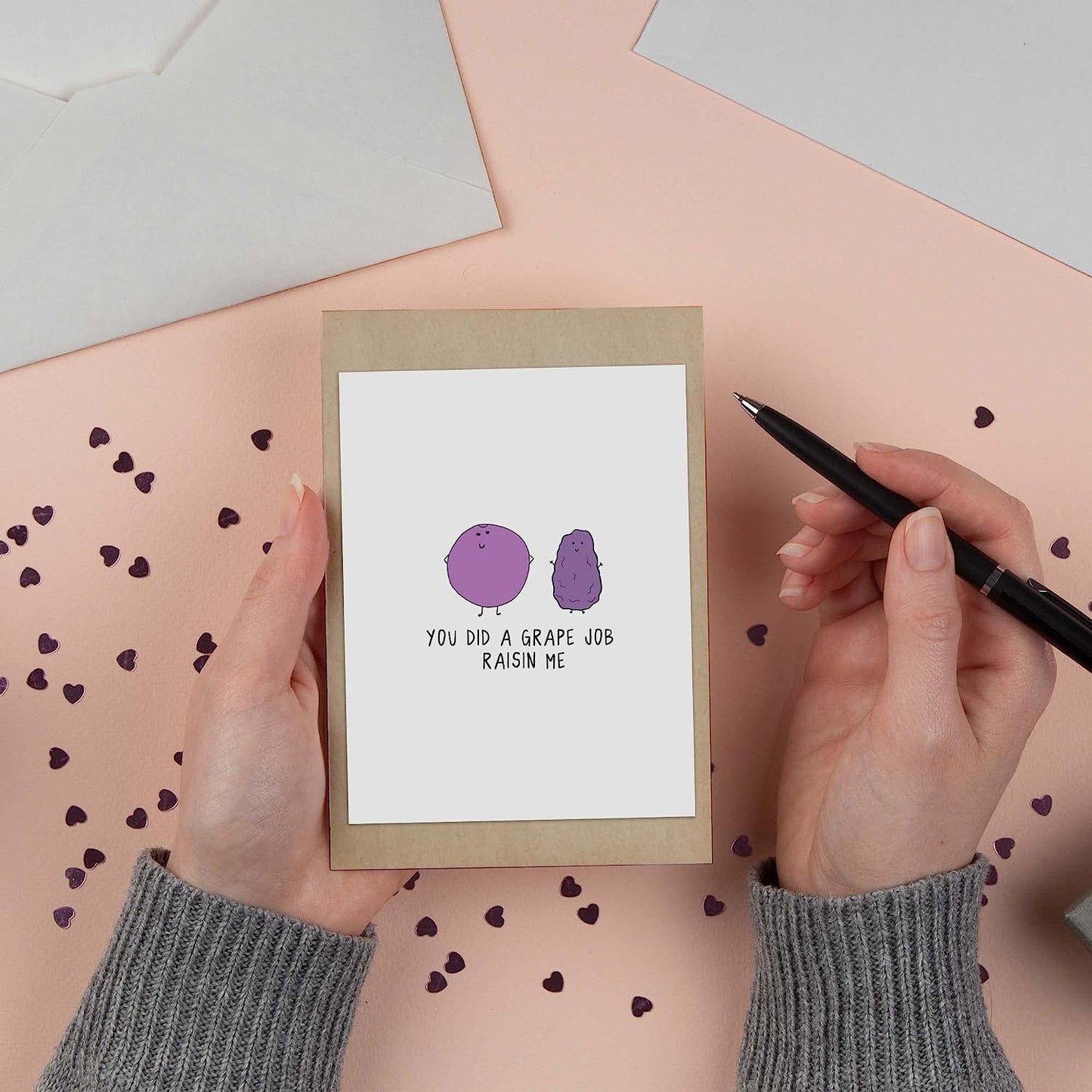 A woman is holding a "Grape Job Raisin Me Card" with a purple dot on it.