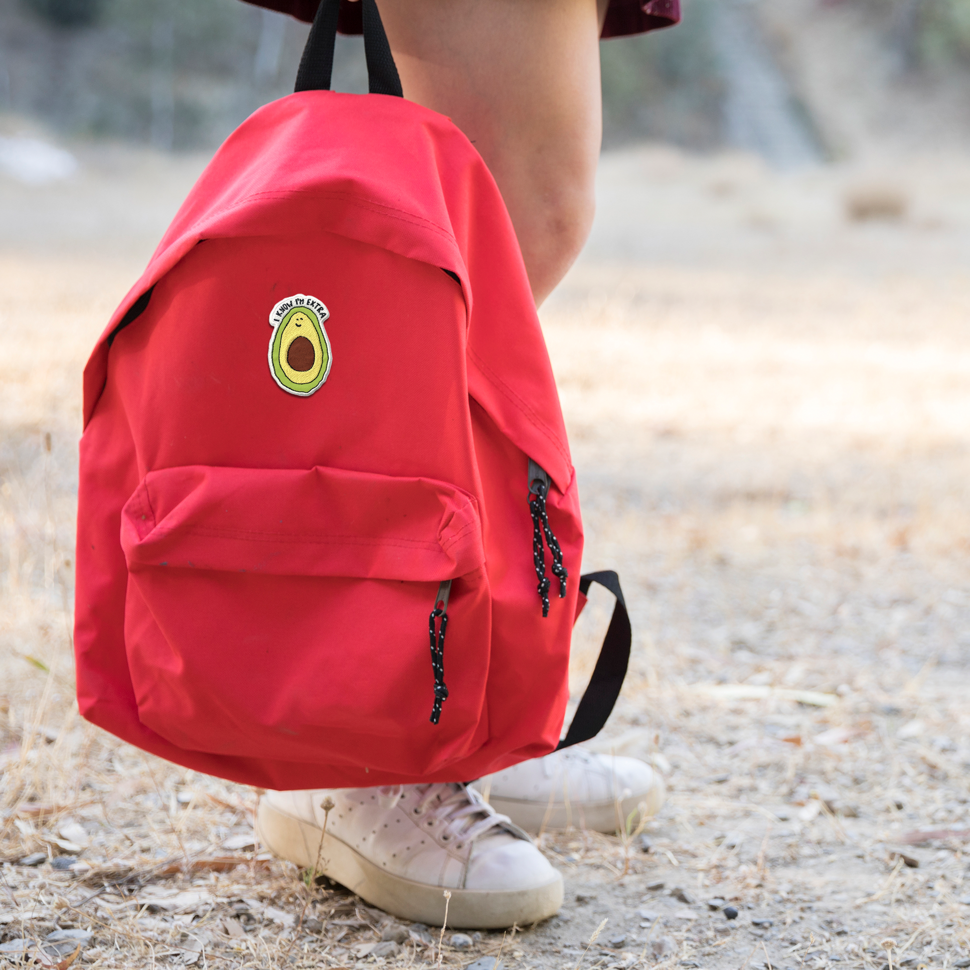 A girl wearing a red backpack with the "I Know Im Extra" patch by rockdoodles, featuring an acorn embroidered on it.