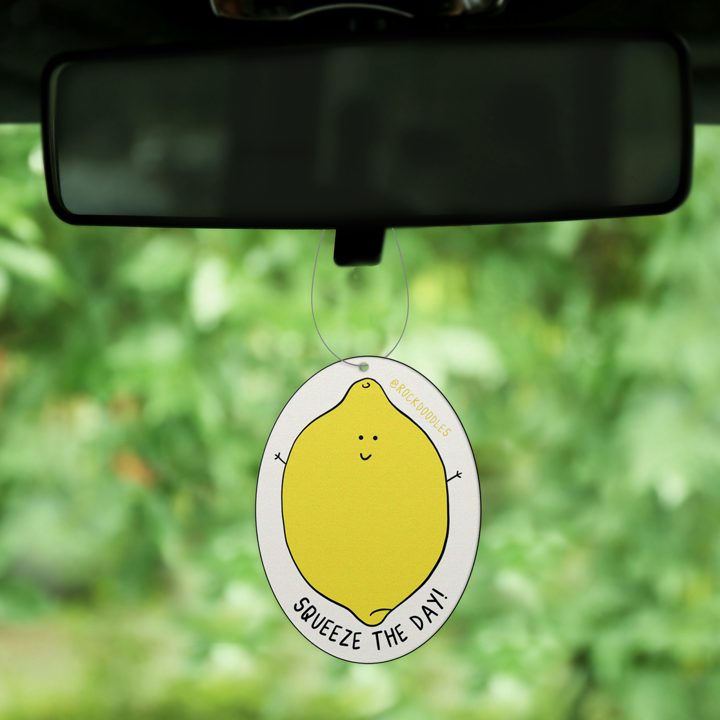 A Squeeze The Day (2-Pack) Punny Air Freshener - Lemon Scent by rockdoodles hangs from a car window.