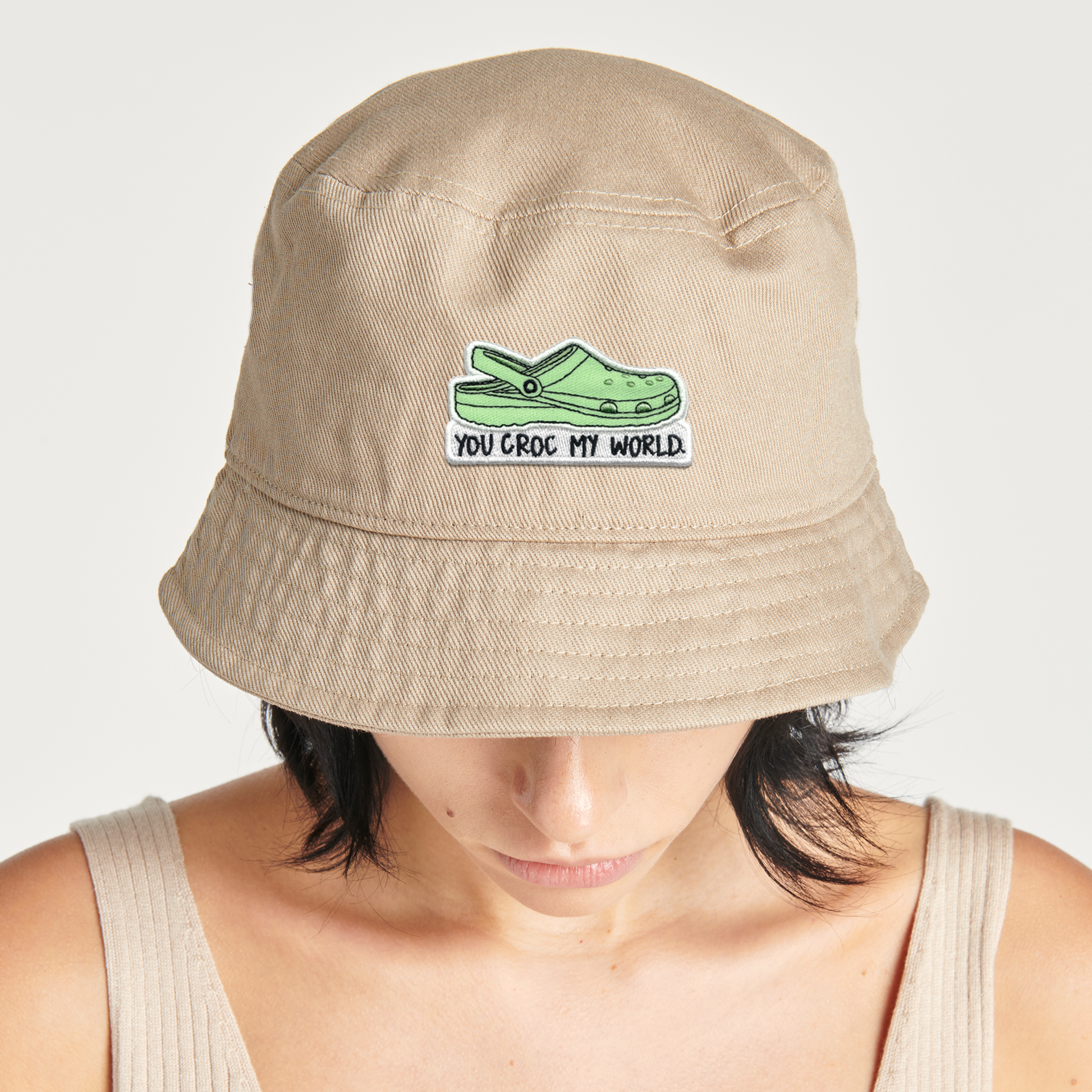 A woman wearing a tan bucket hat with a green rockdoodles You Croc My World Patch.