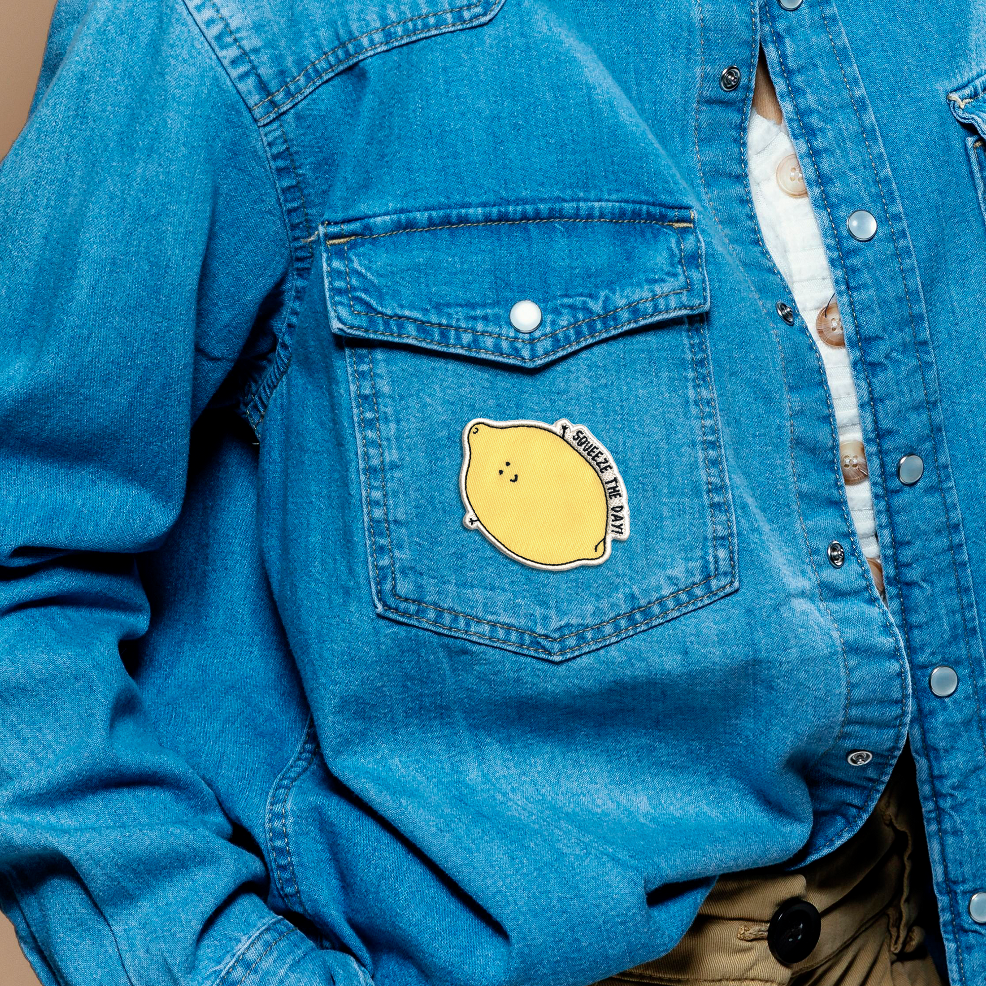 A woman wearing a blue denim jacket adorned with a rockdoodles Squeeze The Day Patch, following iron-on instructions using a household iron.