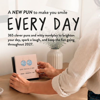 A person flips a page on the 2027 A Pun A Day Desktop Calendar by rockdoodles, revealing a pun-filled illustration with witty wordplay. Set against modern decor and a flower vase, this charming, plastic-free calendar features 365 unique puns and clever drawings—one for every day of the year.