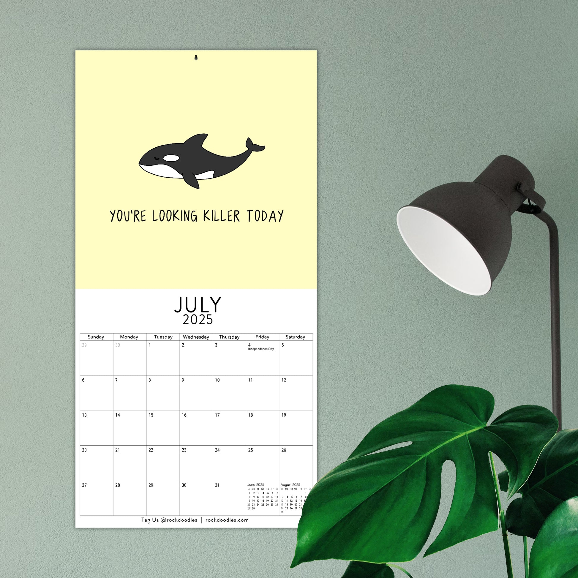 Set to July 2025, the "You've Got To Be Yolking" wall calendar from rockdoodles features an illustration of an orca with the text "You're looking killer today." Nearby, you'll find a black lamp and green plant. This Rockdoodles calendar showcases vibrant design and pun-filled fun.