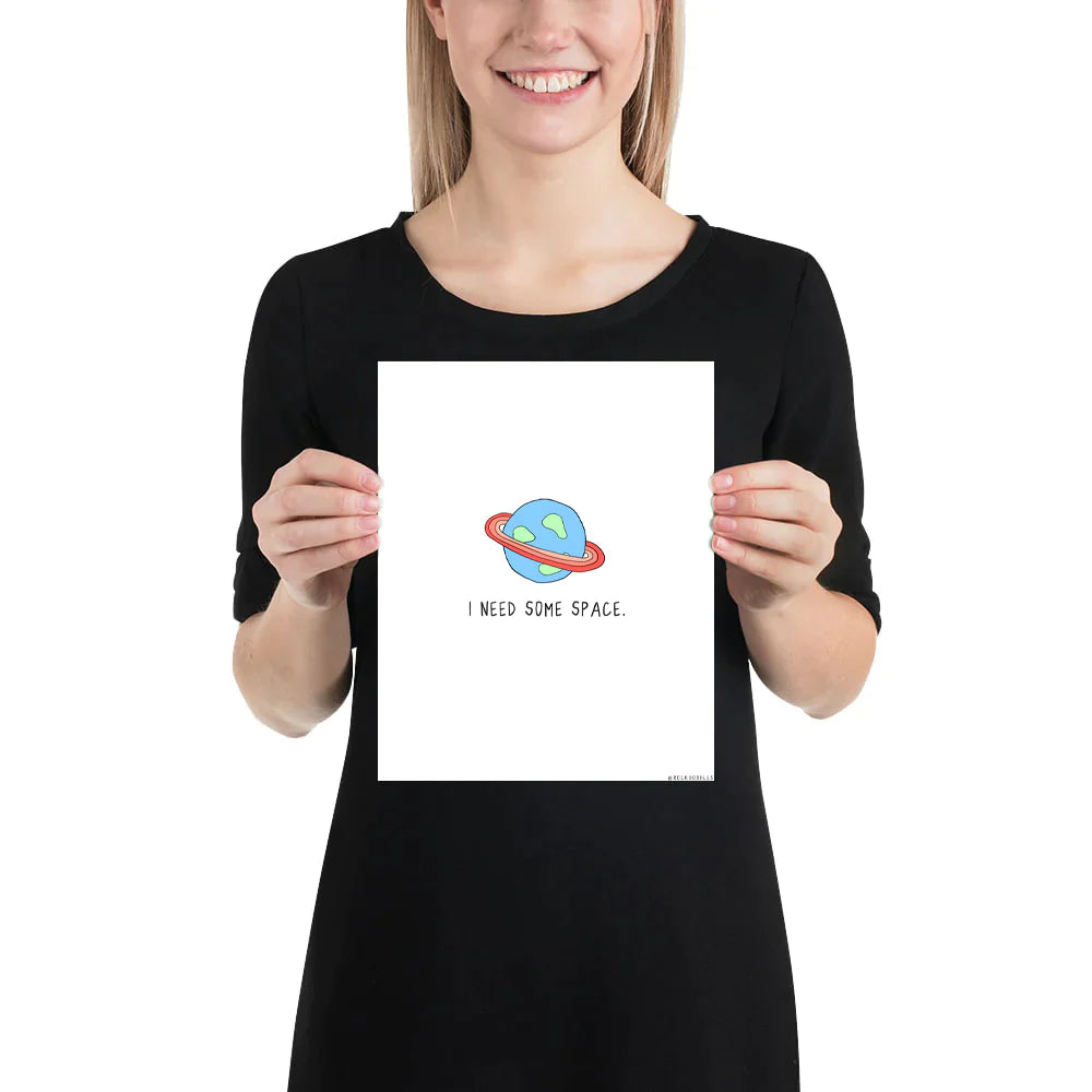 A woman holding up a framed poster that says "I Need Space Print" by rockdoodles.