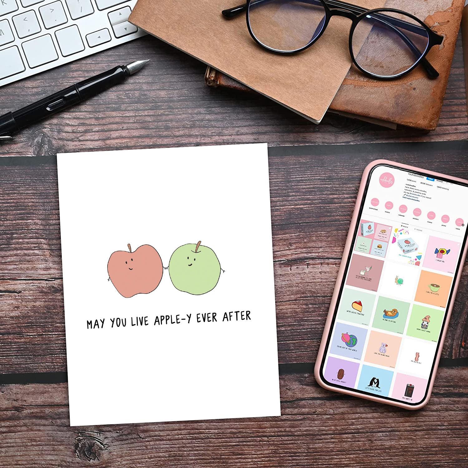 A desk with a phone and a notepad featuring an Apple-y Ever After Card by rockdoodles SEO keyword.